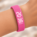Réveil bracelet vibrant rose porté au poignet avec affichage numérique blanc