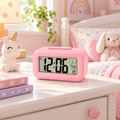 Réveil numérique enfant rose avec grands chiffres posé sur une table de chevet